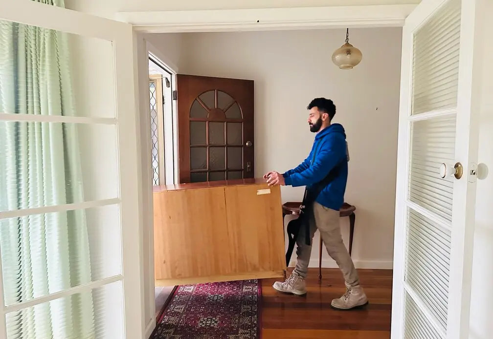 A House Removalists Melbourne crew member carrying a timber sideboard out through the front rooms of a Melbourne home