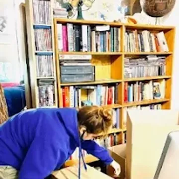 A crew member packing a full bookshelf into cartons